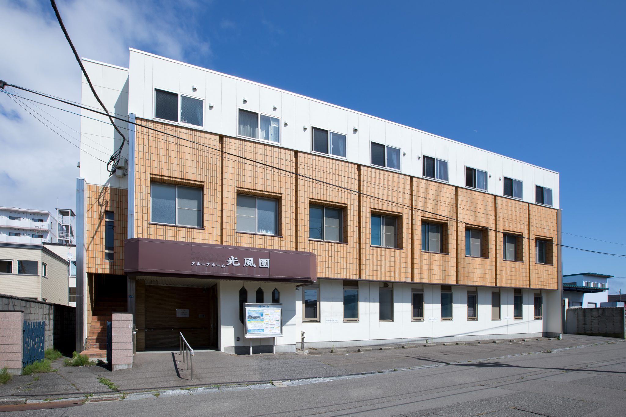 木調タイル張りの現代的な介護施設の建物外観。玄関前の広場あり