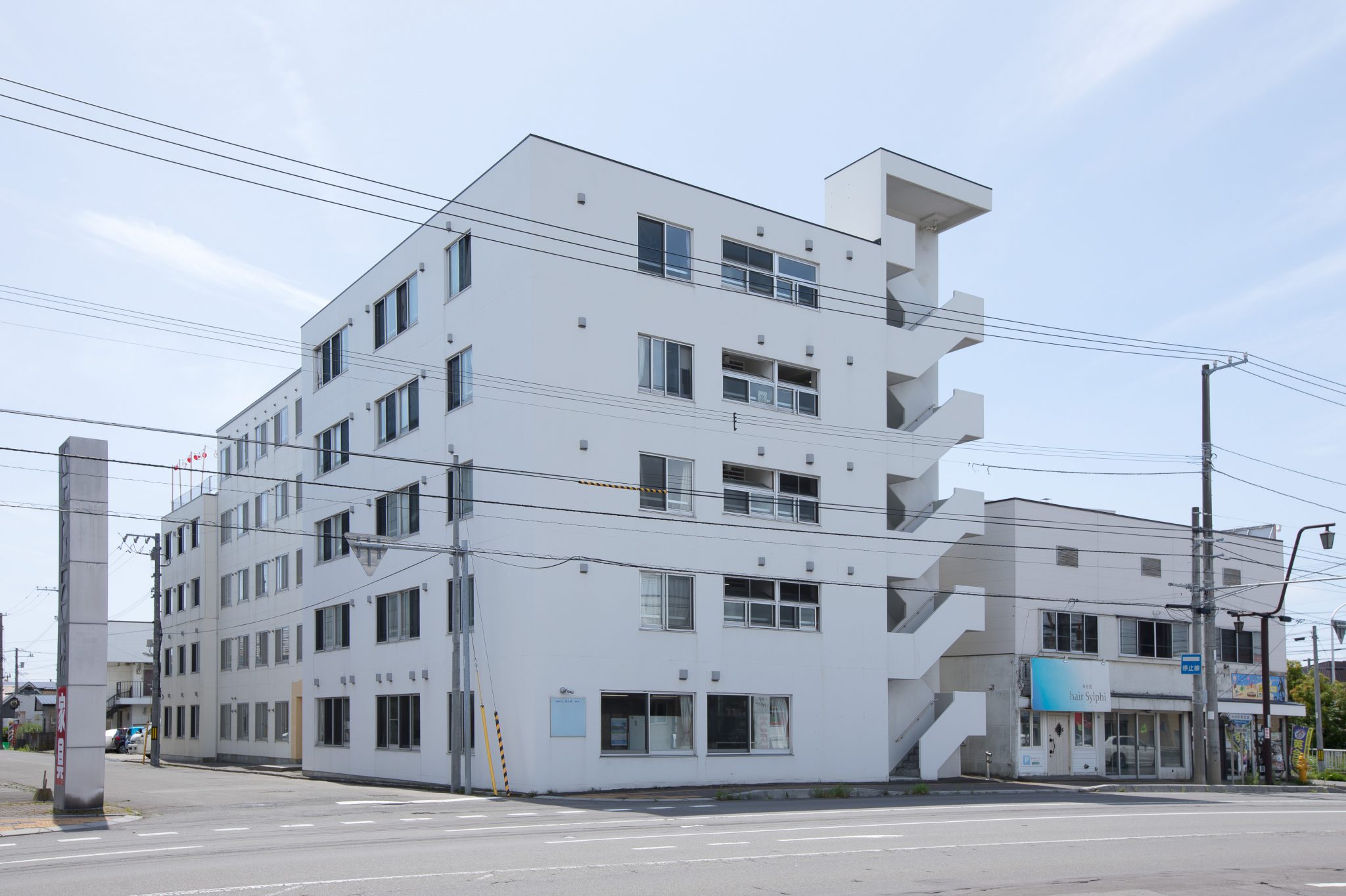 白色5階建ての介護施設建物外観。バルコニー付きの現代的な建築。